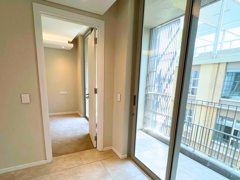 A bright, modern hallway featuring tiled flooring, recessed lighting, and a sliding glass door providing access to an outdoor balcony area.