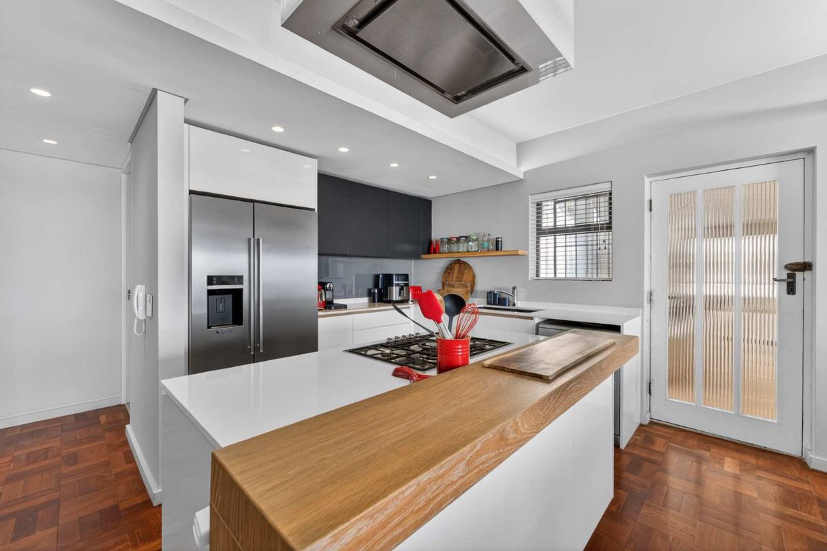 Modern kitchen featuring a gas hob, stainless steel extractor, stone countertops with a timber breakfast bar, and elegant parquet flooring.