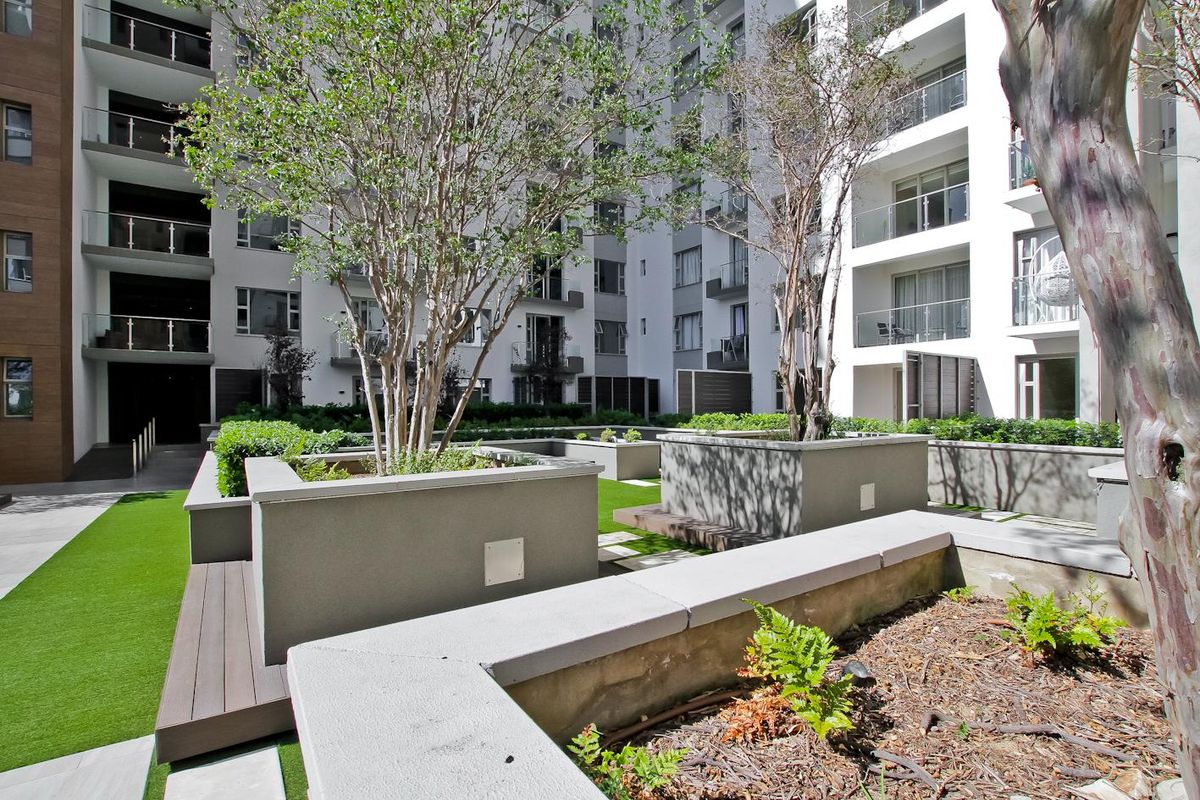 A well-maintained communal courtyard area featuring raised concrete planters, synthetic lawn, and integrated timber bench seating within an apartment complex.