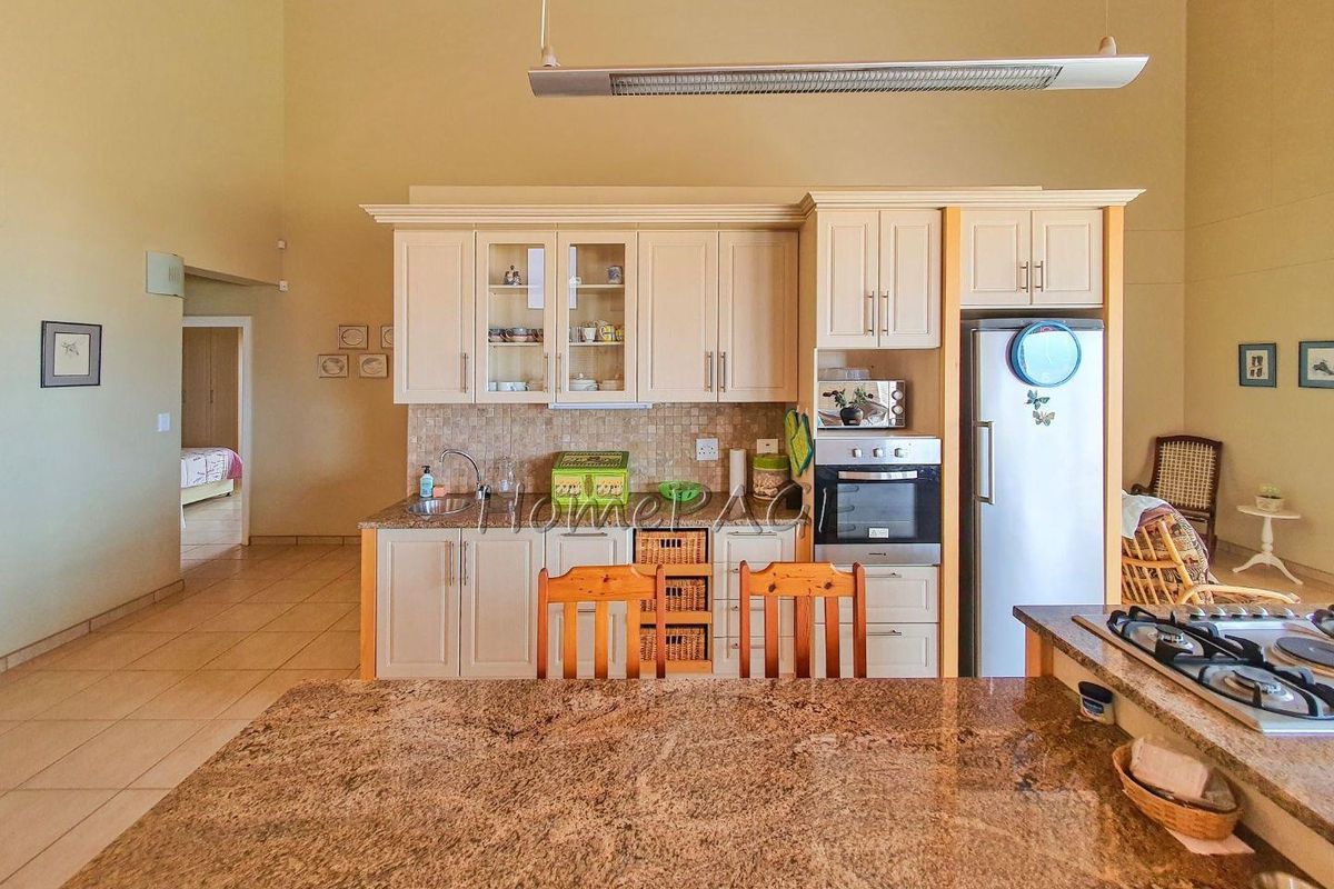 A spacious kitchen featuring granite countertops, built-in cabinetry, an integrated oven, and a central island with a gas hob.