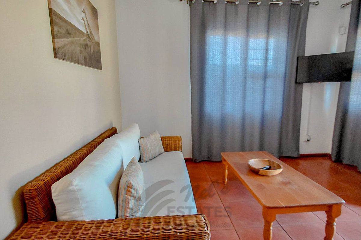 A comfortable living room area featuring tiled flooring and large windows with curtains, providing a functional space for relaxation.