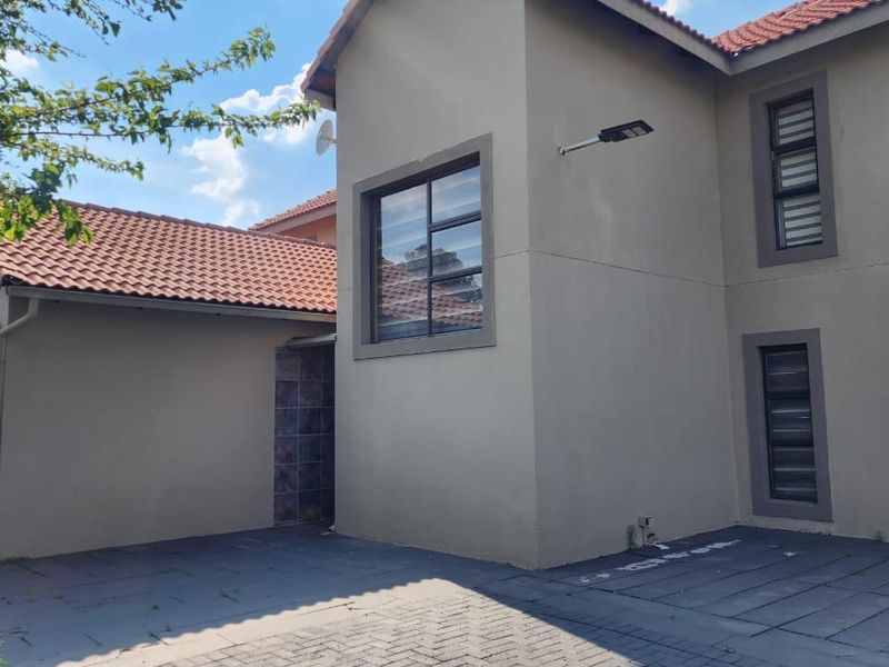 Front exterior view of a townhouse featuring a paved driveway, tiled roof, and modern aluminium window frames.