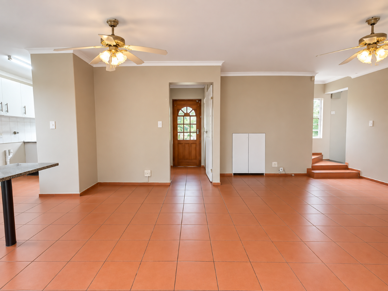 Spacious open-plan living area featuring terracotta-style floor tiles, dual ceiling fans, and direct access to the kitchen and main entrance.