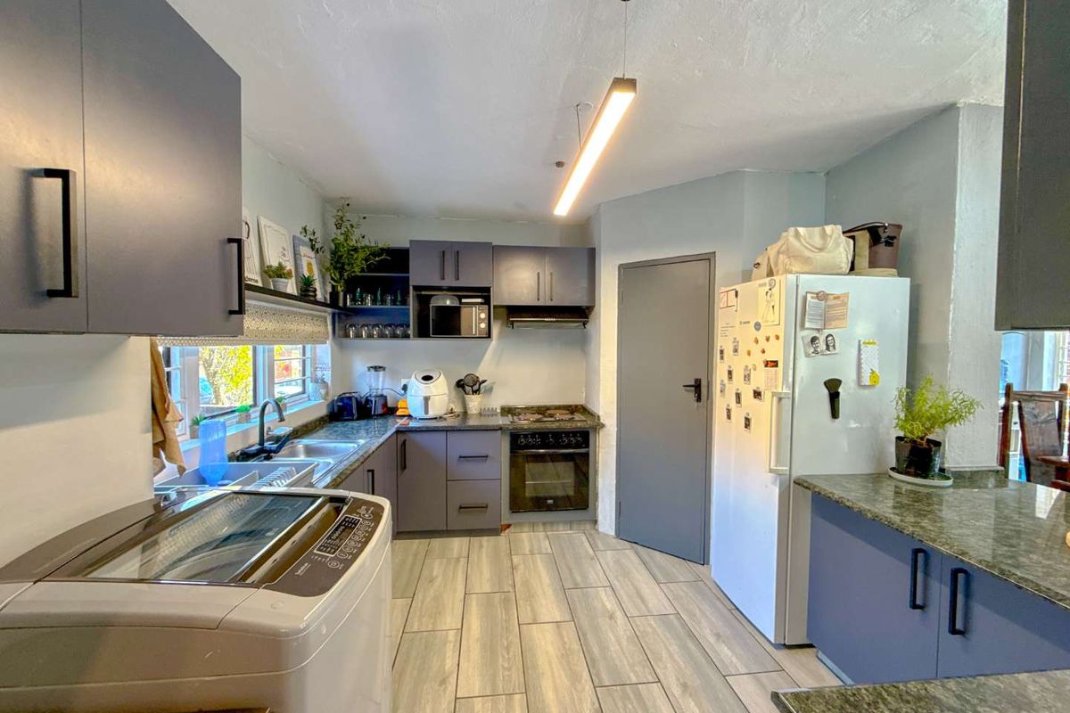 A functional kitchen featuring dark grey cabinetry, granite countertops, integrated oven and hob, and modern tiled flooring with ample storage space.
