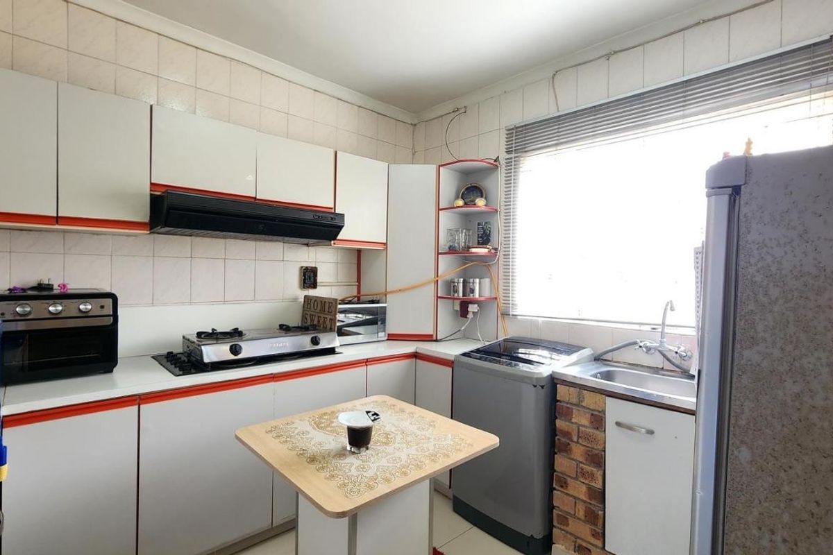 A functional kitchen featuring built-in cabinetry, a gas hob with extractor fan, tiled splashback, and a stainless steel sink with exposed brick detailing.