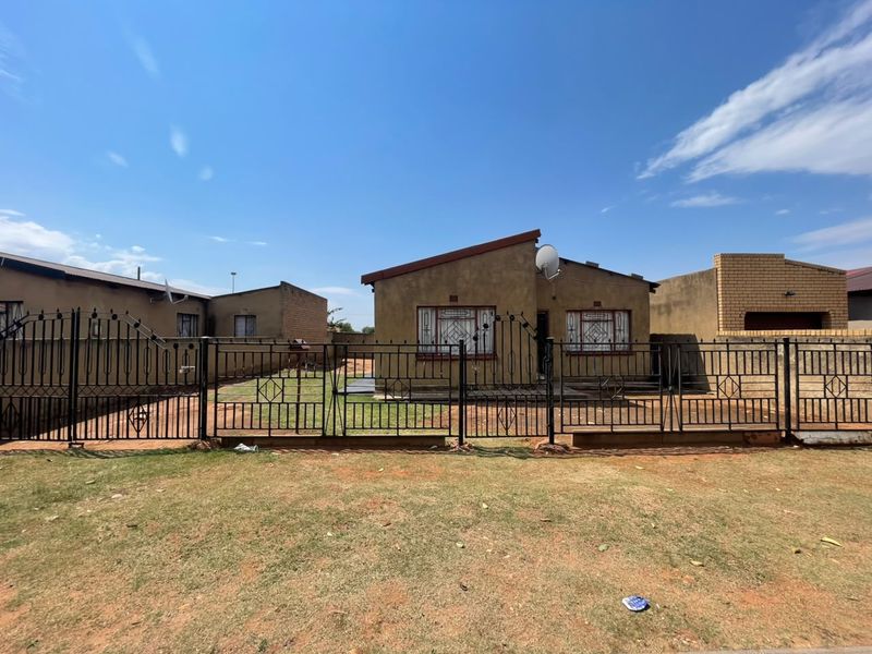 Front view of a single-story residential house featuring metal security fencing, security bars on windows, and a satellite dish.