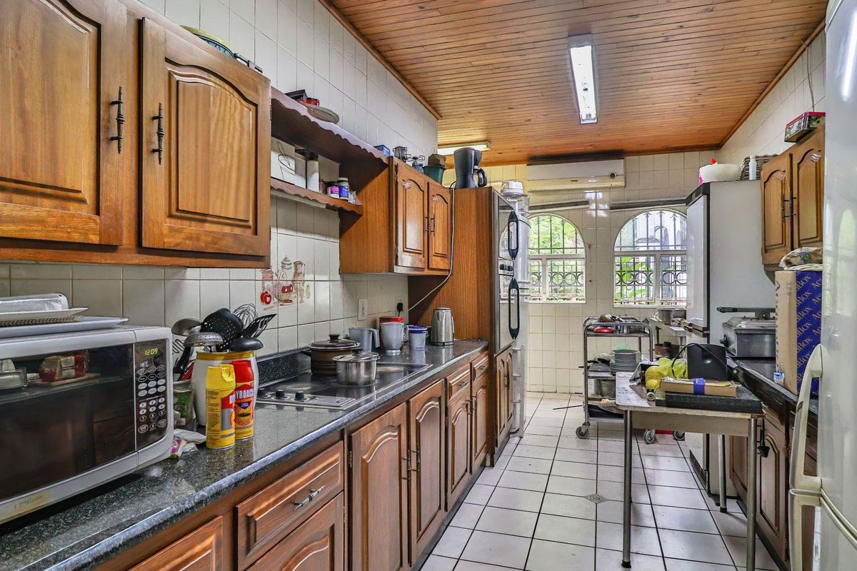 A functional kitchen featuring wooden cabinetry, granite countertops, tiled walls, and a timber-paneled ceiling with integrated lighting.