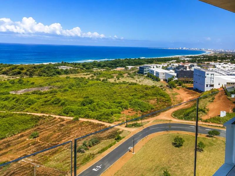 Elevated balcony view overlooking coastal landscape, green fields, and the ocean, featuring a modern glass balustrade.