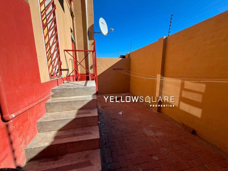 A paved rear courtyard area featuring a boundary wall with electric fencing, concrete steps, and a metal security gate.