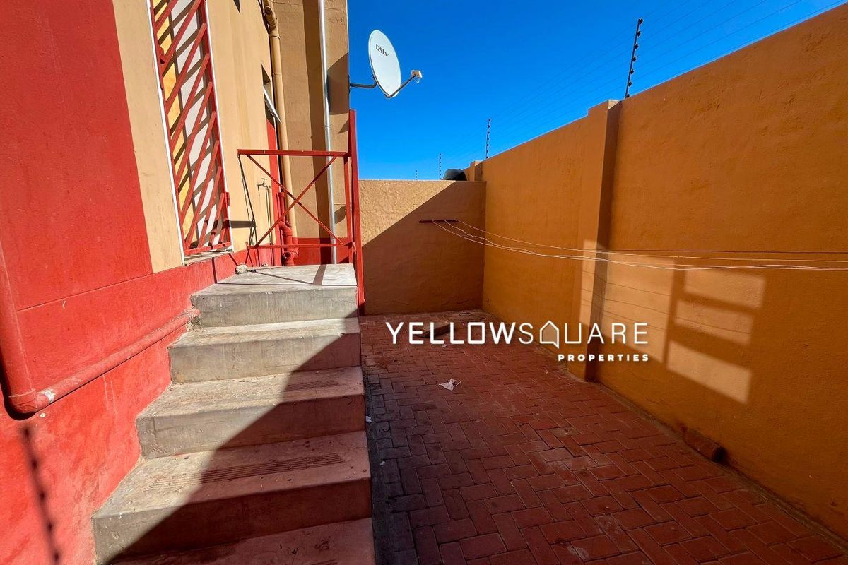 A paved rear courtyard area featuring a boundary wall with electric fencing, concrete steps, and a metal security gate.