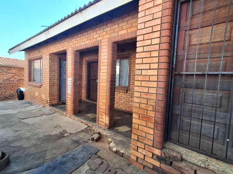 Rear exterior view of a face brick house featuring a covered patio area with security gates and concrete paving.
