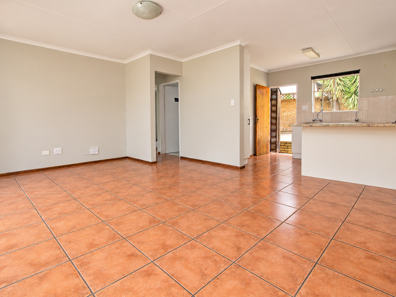 Spacious open-plan living area featuring terracotta-style floor tiles, a functional kitchen with breakfast bar, and direct access to an outdoor patio area.