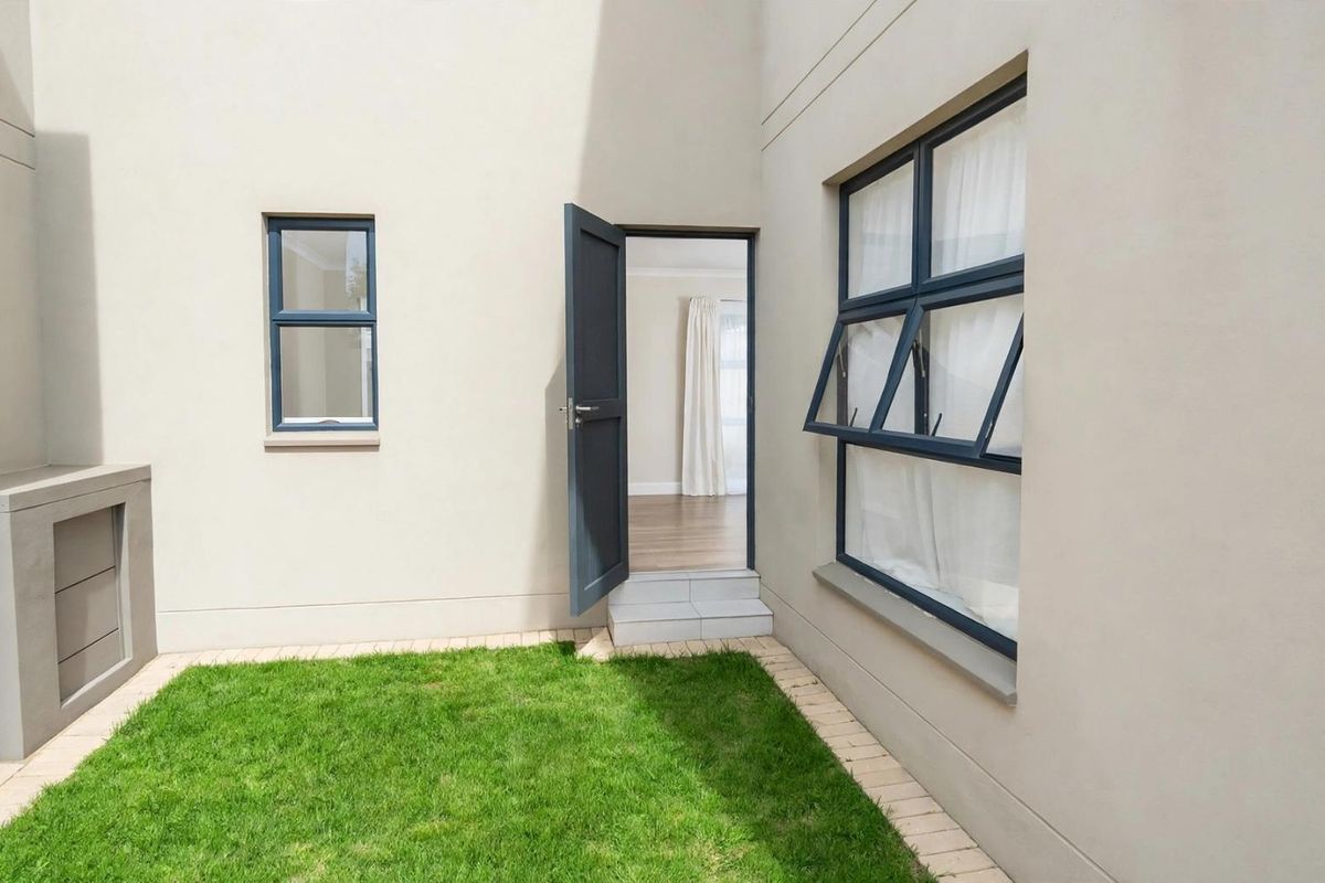 A neat rear courtyard featuring a small lawn, built-in outdoor counter, and direct access to the interior living space through a side door.