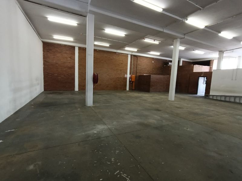 Spacious industrial warehouse area featuring exposed brick walls, concrete flooring, and functional overhead fluorescent lighting, suitable for various commercial or storage applications.