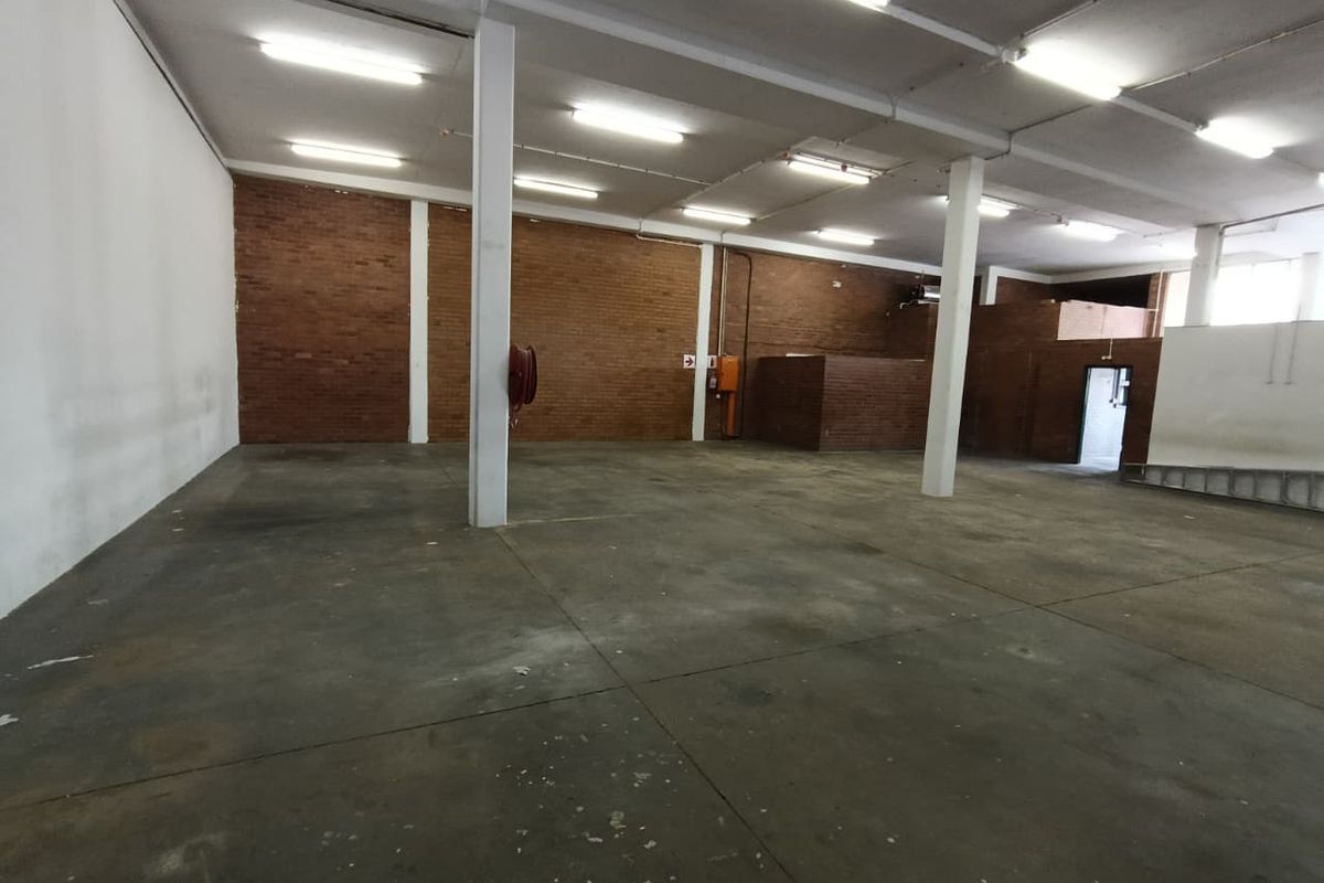 Spacious industrial warehouse area featuring exposed brick walls, concrete flooring, and functional overhead fluorescent lighting, suitable for various commercial or storage applications.