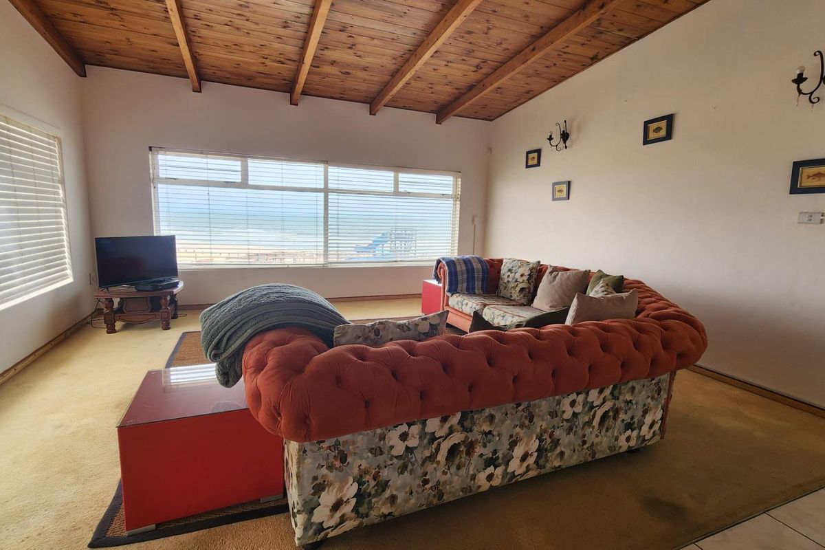 Spacious living room featuring an exposed timber beam ceiling, large windows with ocean views, and wall-mounted lighting, offering a comfortable coastal living space.