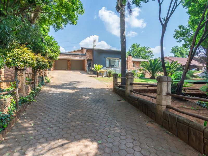 Front view of the property featuring a paved driveway leading to a double garage, surrounded by a landscaped garden and stone-accented fencing.