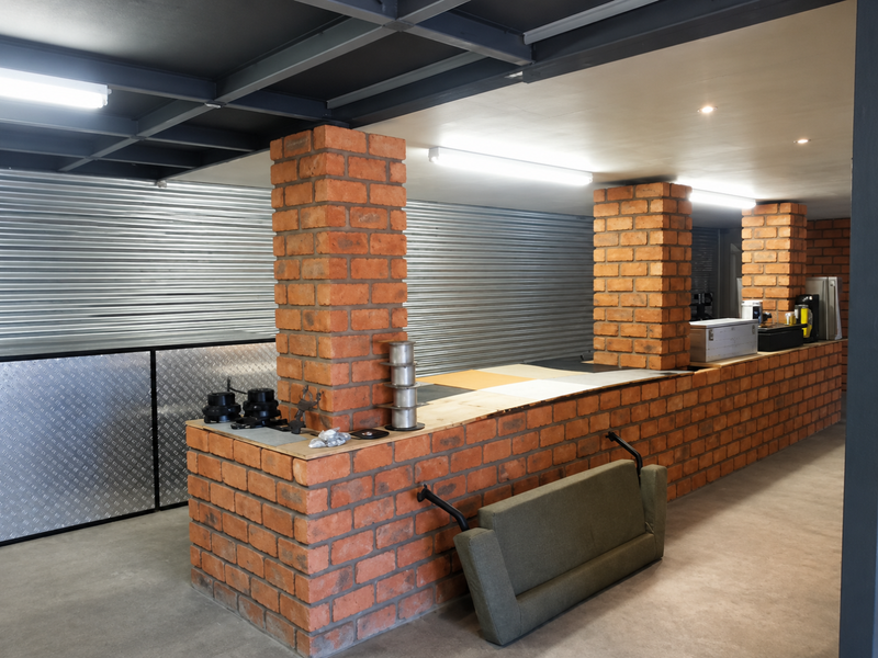 Industrial utility space featuring exposed steel beams, brick columns, corrugated metal wall cladding, and durable concrete flooring with integrated strip lighting.