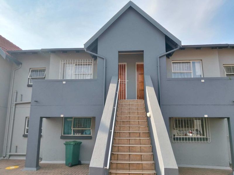Front elevation of a townhouse complex featuring a central tiled staircase leading to upper-level entrances with security bars and grey painted exterior walls.