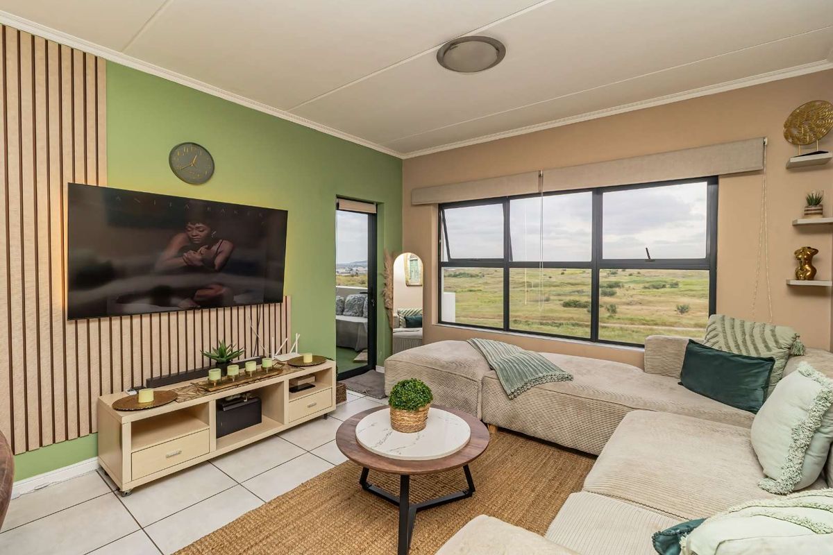 A bright living room featuring modern slat wall paneling, large windows with scenic views, and neutral tiled flooring.