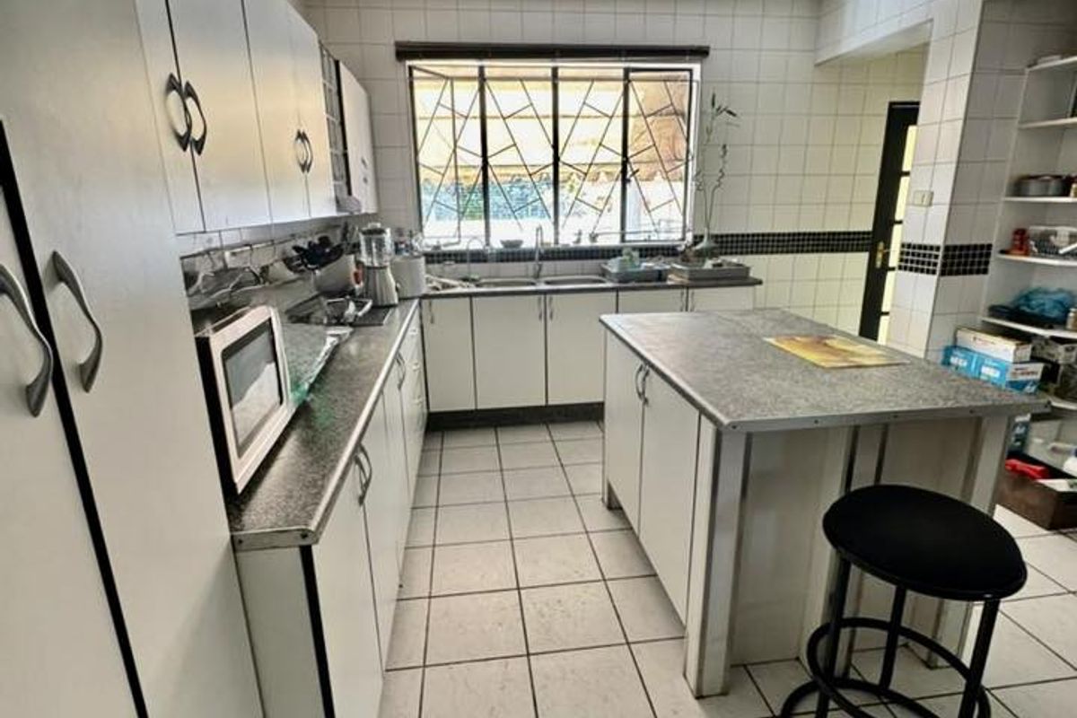 A functional kitchen featuring white cabinetry, a central island, tiled flooring, and a built-in ceiling light panel with a window overlooking the exterior.