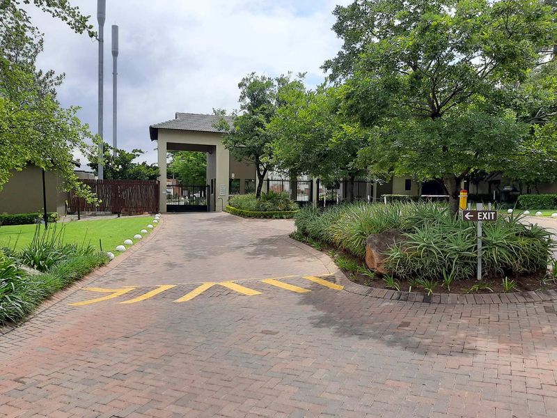 The entrance to the apartment complex features a paved driveway, a secure gatehouse, and well-maintained landscaped gardens.