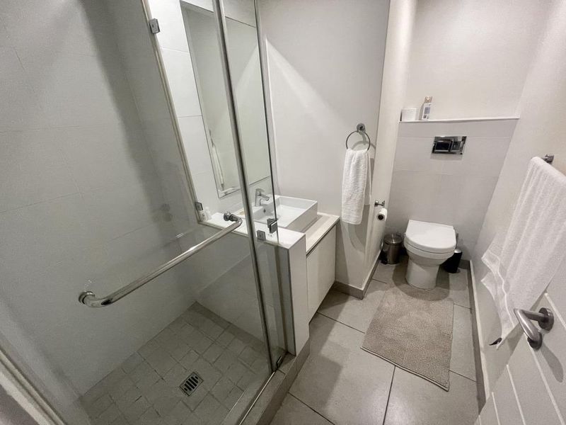 A compact, modern bathroom featuring a glass-enclosed shower, a vessel sink vanity, and a wall-mounted toilet with concealed cistern.
