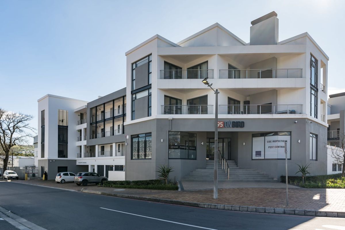Modern multi-story apartment building facade featuring balconies, a paved entrance area, and contemporary architectural design.