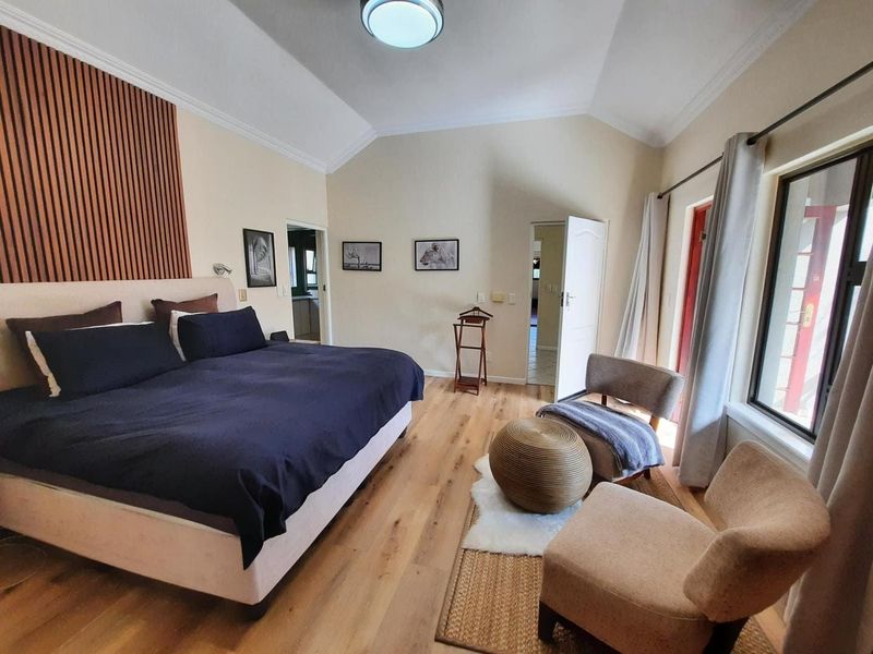 Spacious bedroom featuring vaulted ceilings, timber flooring, and a decorative slat wall panel, with direct access to an outdoor area.