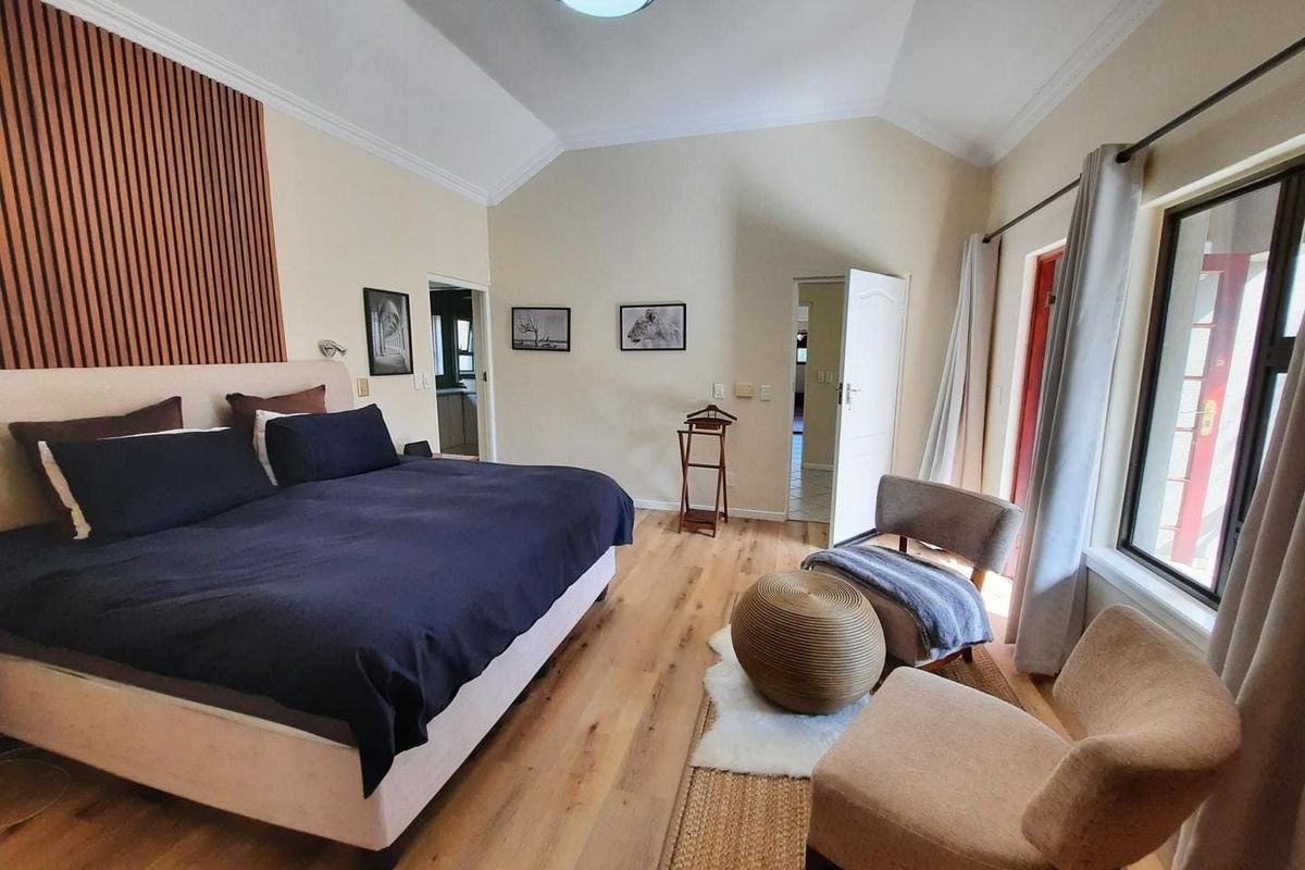 Spacious bedroom featuring vaulted ceilings, timber flooring, and a decorative slat wall panel, with direct access to an outdoor area.
