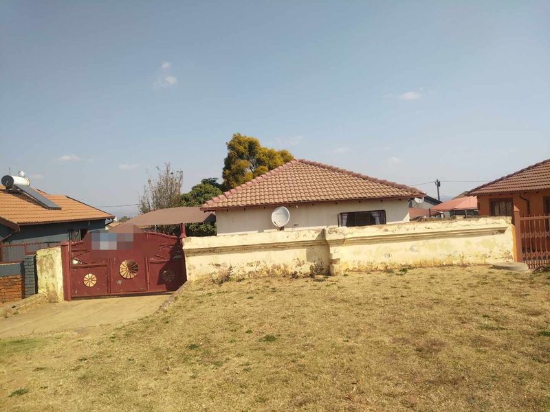 Front view of a residential property featuring a tiled roof, perimeter wall with gate, and solar water heating system.