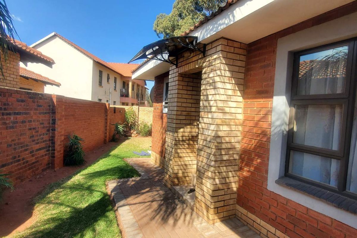 A side view of the house featuring a brick exterior, a paved walkway, and a small garden area with a boundary wall.