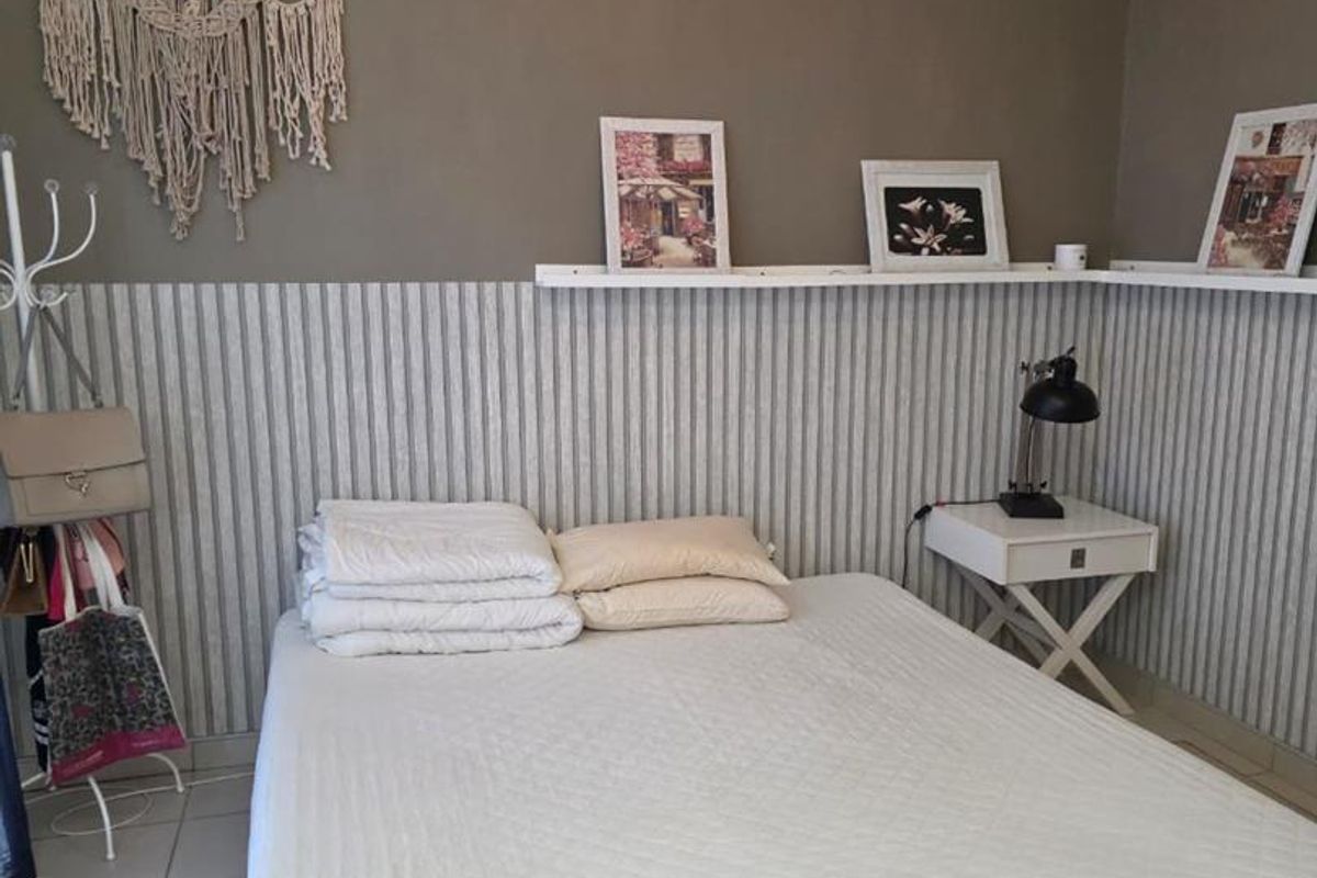 A bedroom featuring wainscoting, wall-mounted shelving, and a ceiling fan, providing a functional space with neutral wall tones.
