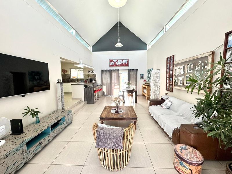 Spacious open-plan living area featuring a high vaulted ceiling, clerestory windows for natural light, tiled flooring, and an integrated kitchen with a breakfast island.