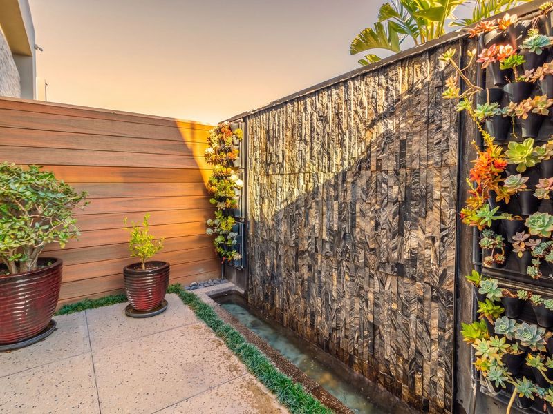 A beautifully landscaped garden area featuring a modern stone water feature, vertical wall planters, and timber privacy screening.
