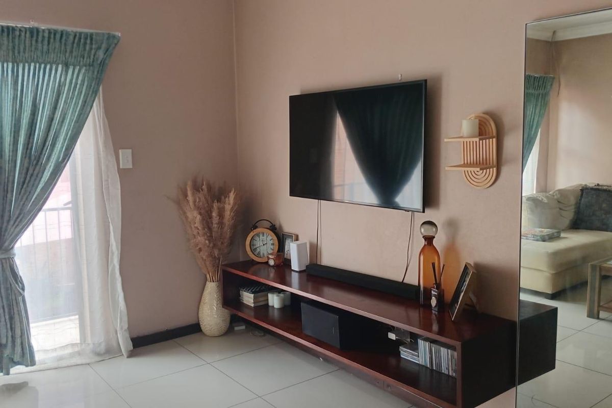 A well-maintained living room featuring tiled flooring, a large wall-mounted mirror, and a sliding glass door providing access to the exterior.