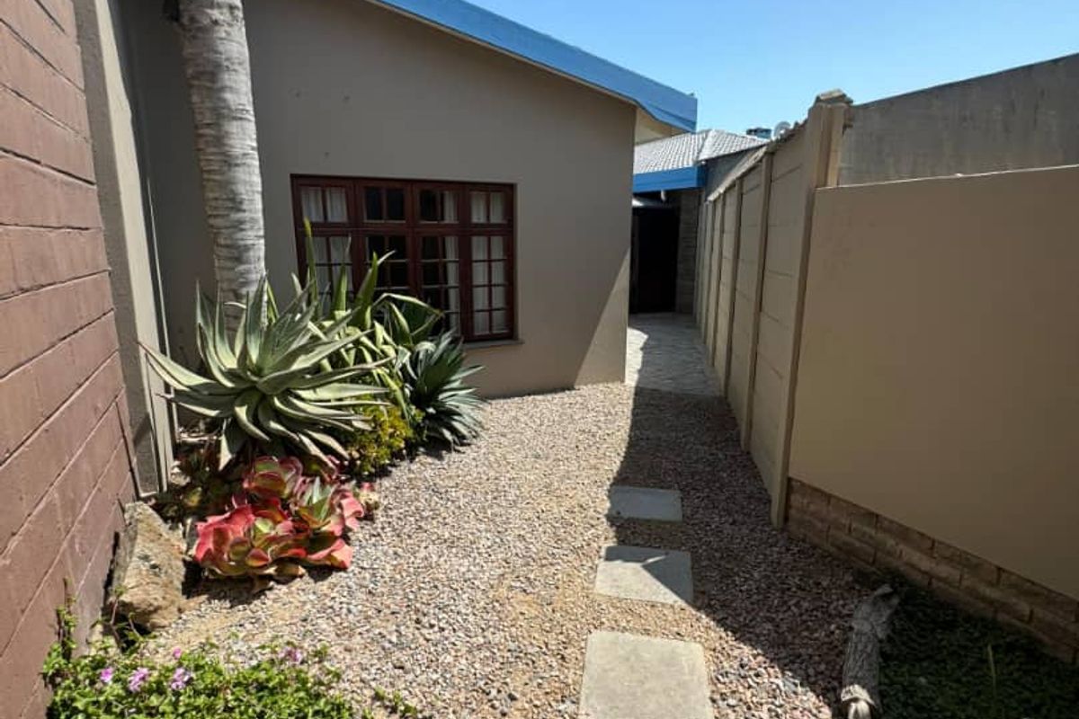 A side passage featuring a gravel pathway with concrete stepping stones, bordered by a precast concrete wall and a brick boundary wall.