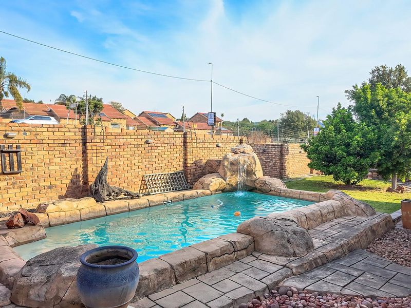 A private outdoor pool area featuring a rock-style waterfall, paved surround, and a secure brick boundary wall within a landscaped garden setting.