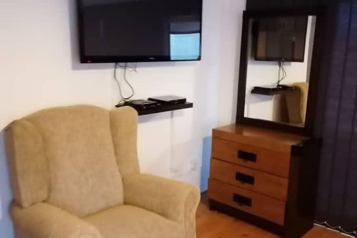 A bedroom interior featuring laminate flooring and a wall-mounted television.
