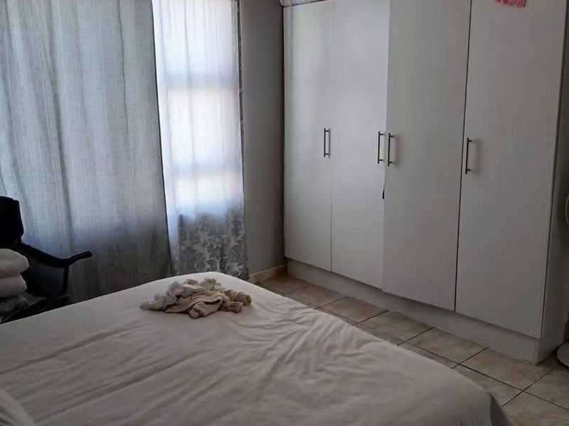 A bedroom featuring tiled flooring and a large white built-in wardrobe providing ample storage space.