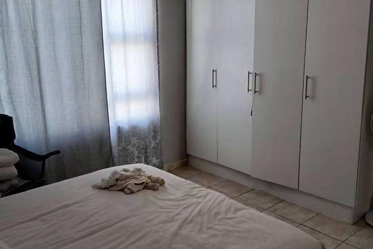 A bedroom featuring tiled flooring and a large white built-in wardrobe providing ample storage space.
