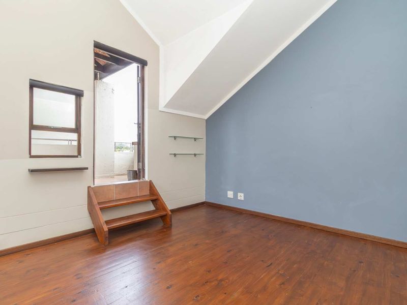 A bedroom featuring wooden flooring, a vaulted ceiling, and a small set of stairs leading to an outdoor balcony area.