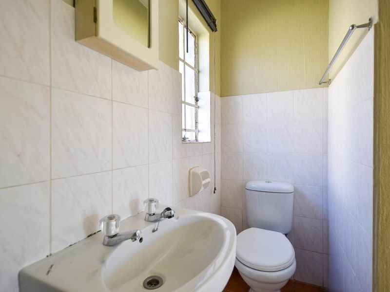 A compact bathroom featuring a pedestal basin, toilet, and tiled walls, requiring cosmetic updates to modernize the space.