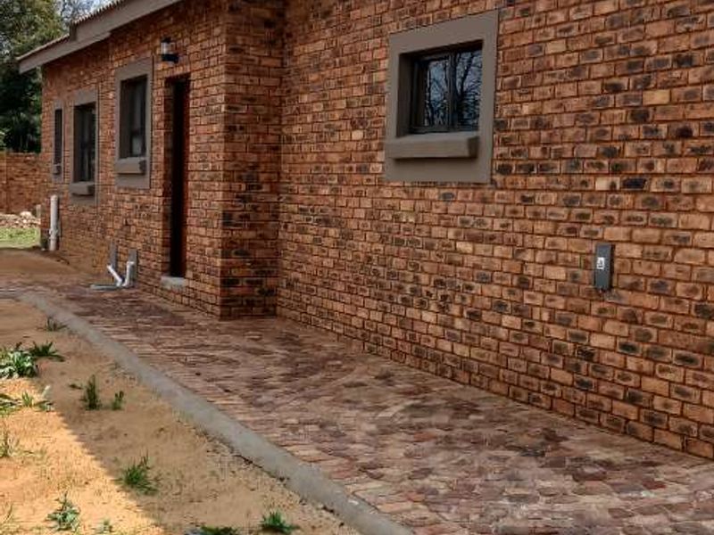 A view of the rear exterior featuring a face brick facade, paved walkway, and aluminium window frames.