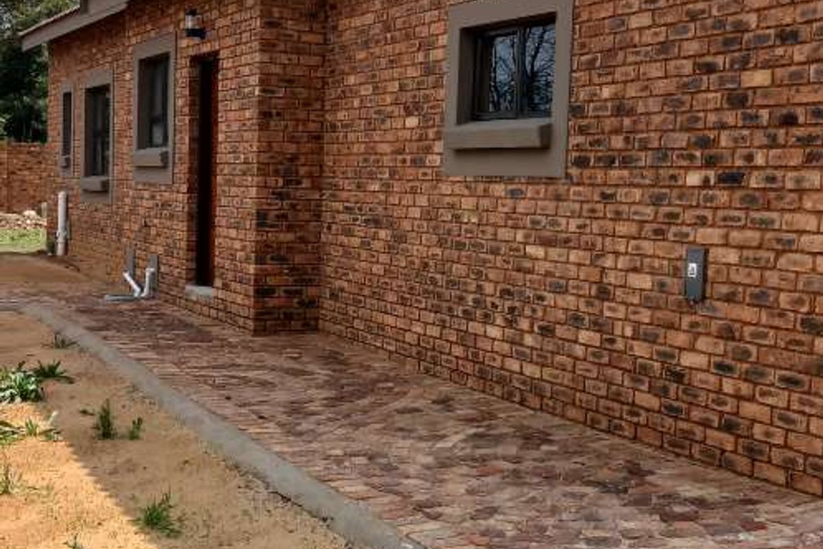 A view of the rear exterior featuring a face brick facade, paved walkway, and aluminium window frames.