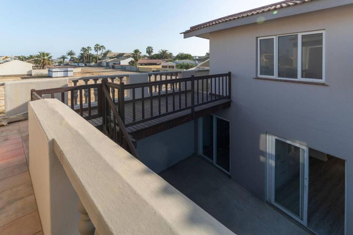 An elevated view of the townhouse exterior, featuring a wooden balcony walkway connecting to the upper level and a paved ground-level patio area.