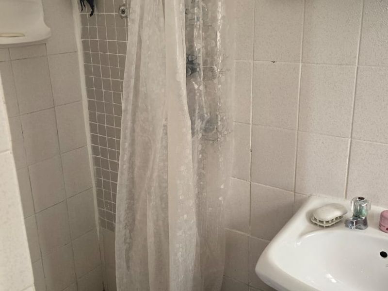 A dated bathroom featuring a pedestal washbasin and a tiled shower area with a curtain rail.
