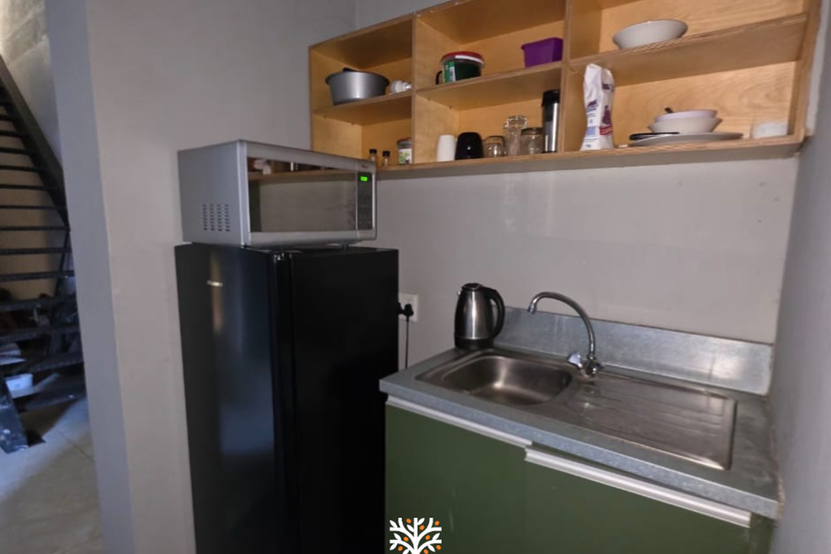 Compact kitchenette area featuring a stainless steel sink, built-in open shelving, and space for a refrigerator.