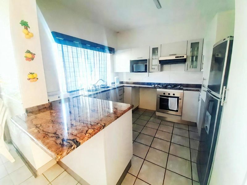 A functional kitchen featuring granite countertops, built-in oven, gas hob, extractor fan, and ample cabinetry with tiled flooring.