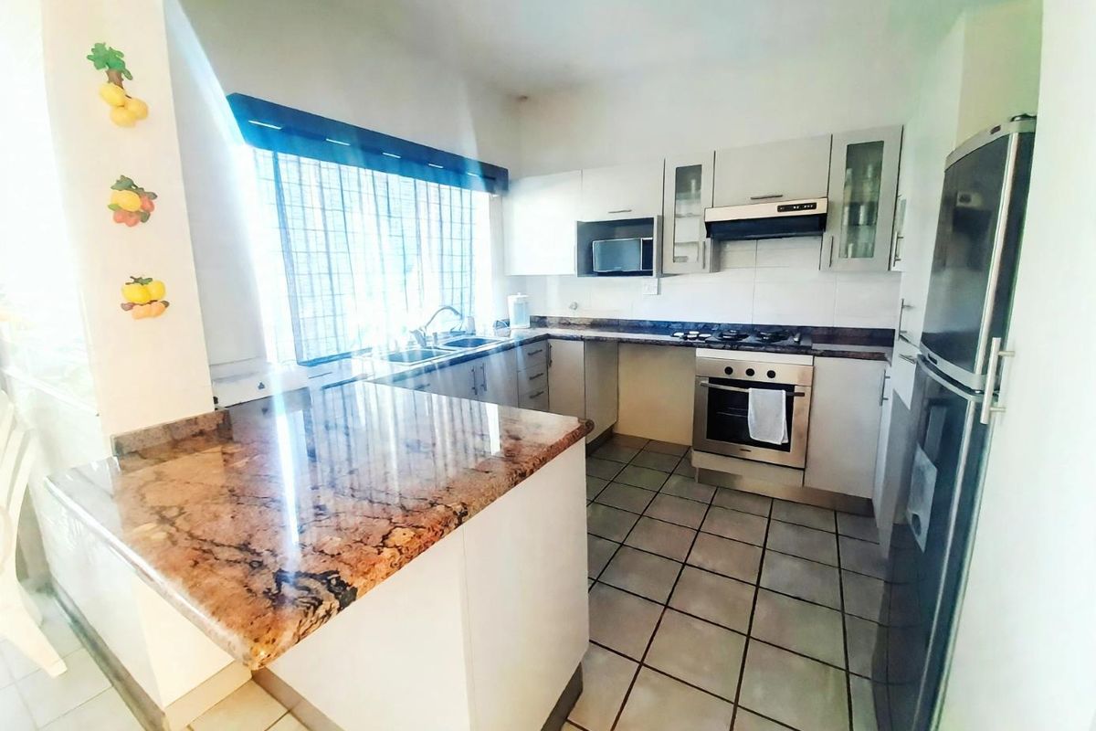 A functional kitchen featuring granite countertops, built-in oven, gas hob, extractor fan, and ample cabinetry with tiled flooring.
